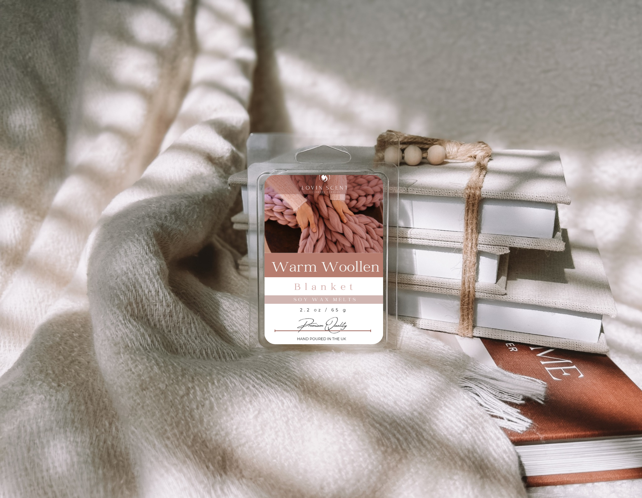 Wax melt packaging labeled 'Warm Woollen' on a stack of books with a blanket
