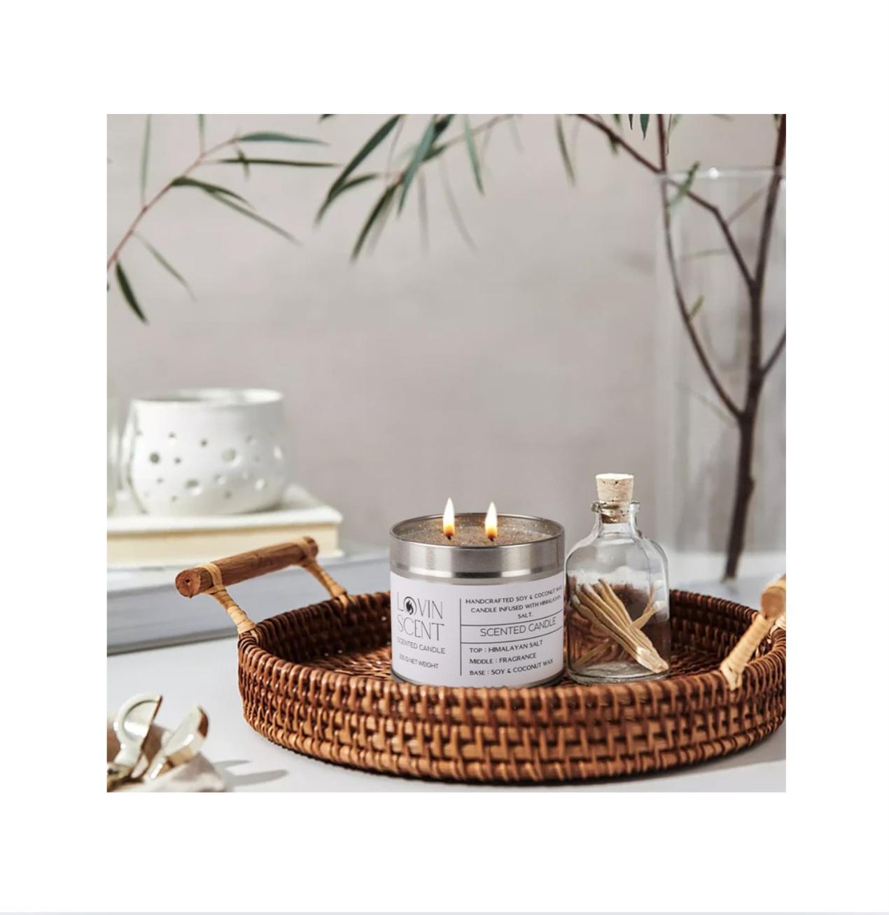 Candle in a metal container on a woven tray with decorative items.