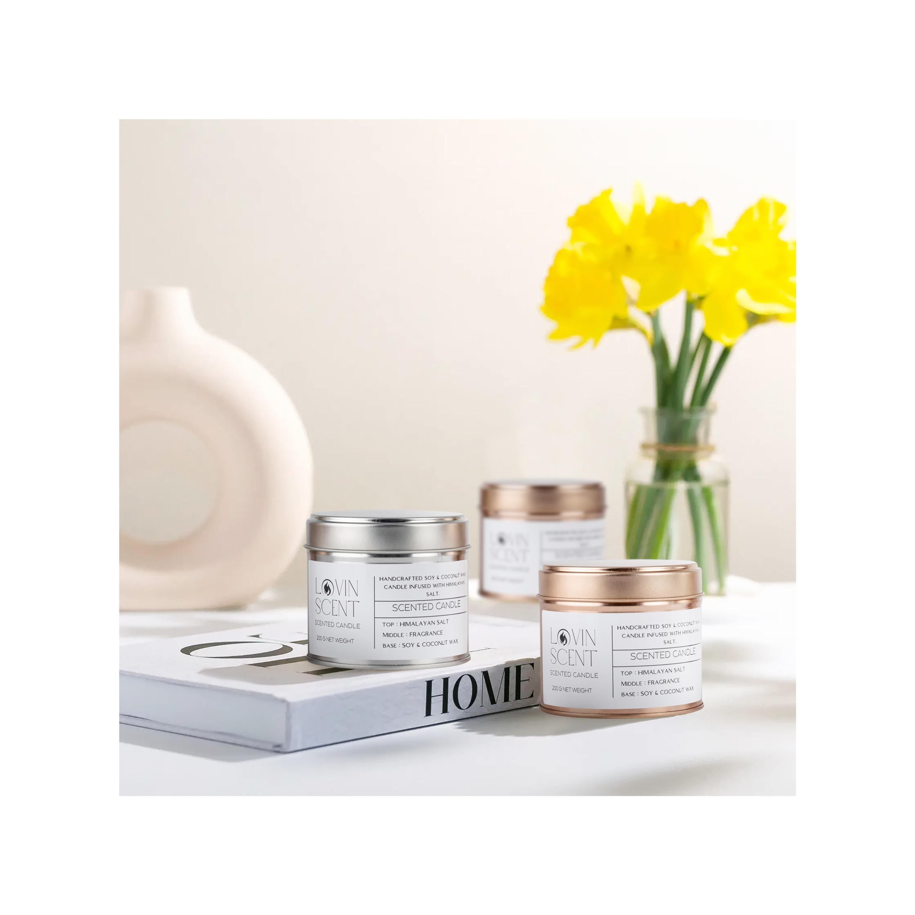 Three candles with gold lids on a white surface with a vase of yellow flowers in the background.