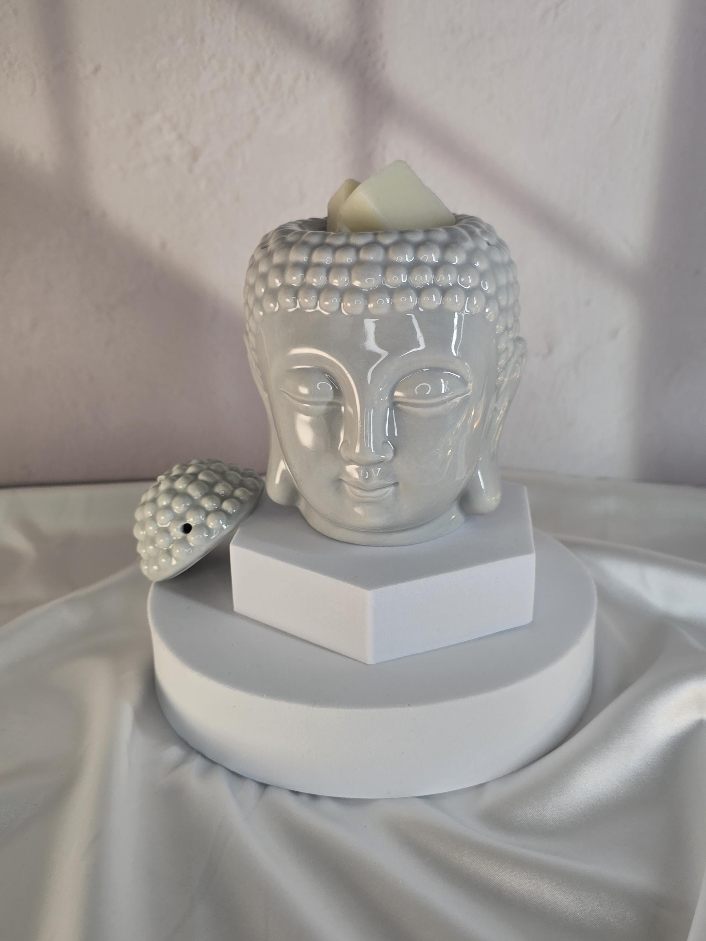 White Buddha head sculpture on a white pedestal with a white background