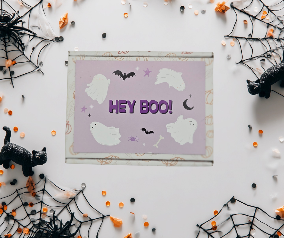 Halloween-themed card with 'HEY BOO!' text surrounded by spider webs, ghosts, and a black cat on a white background.