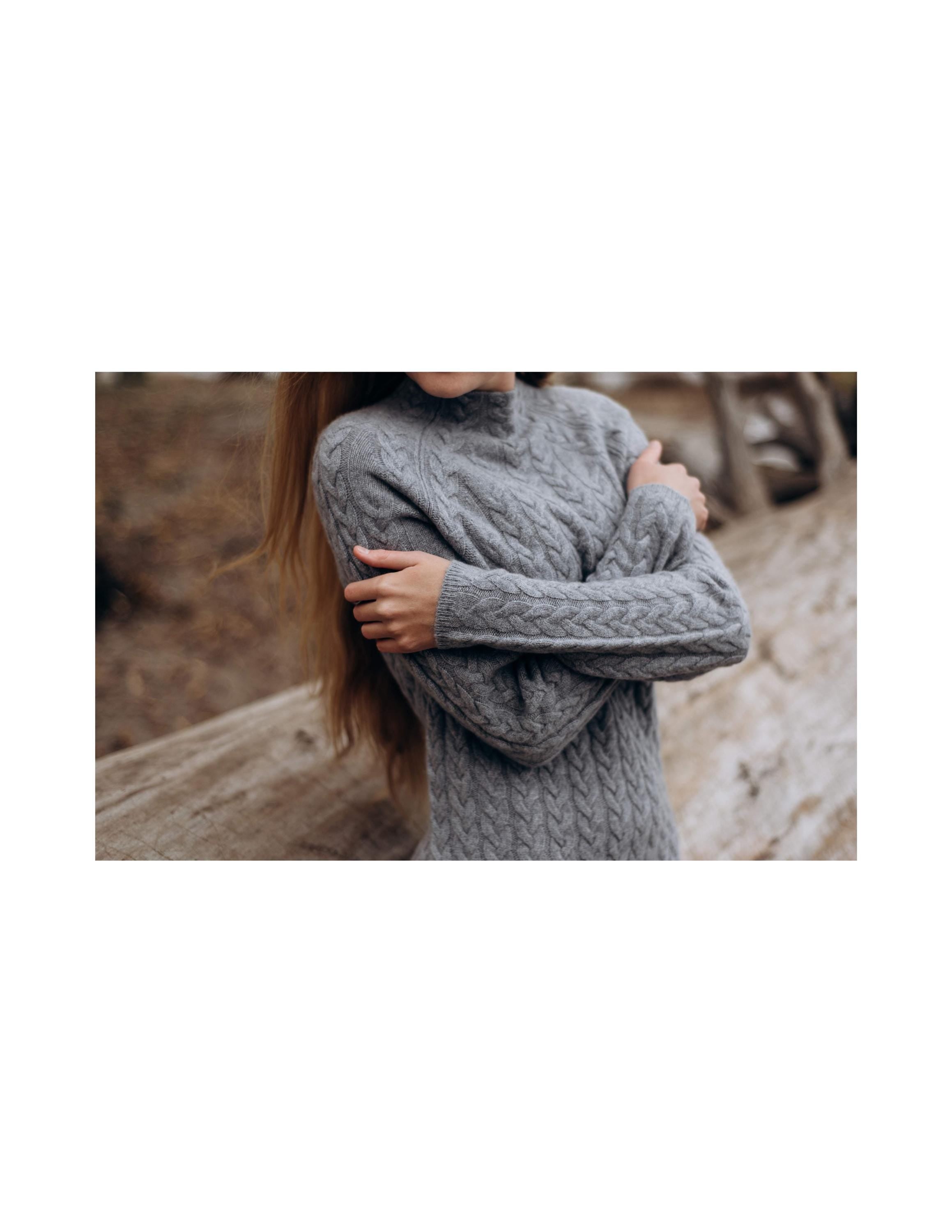 Person wearing a gray knitted sweater with a blurred background