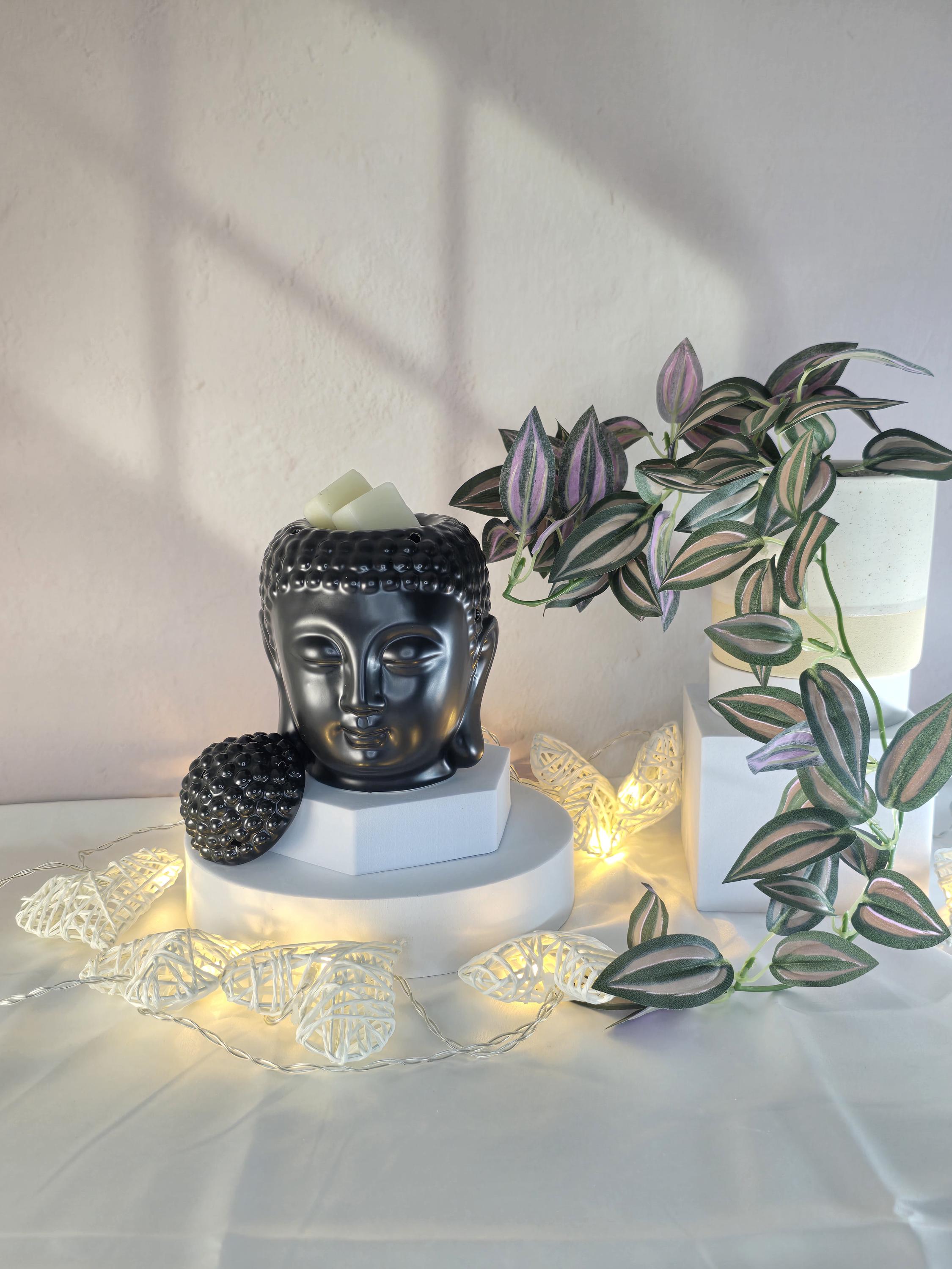 Decorative setup with a Buddha head sculpture, string lights, and a plant on a white surface.