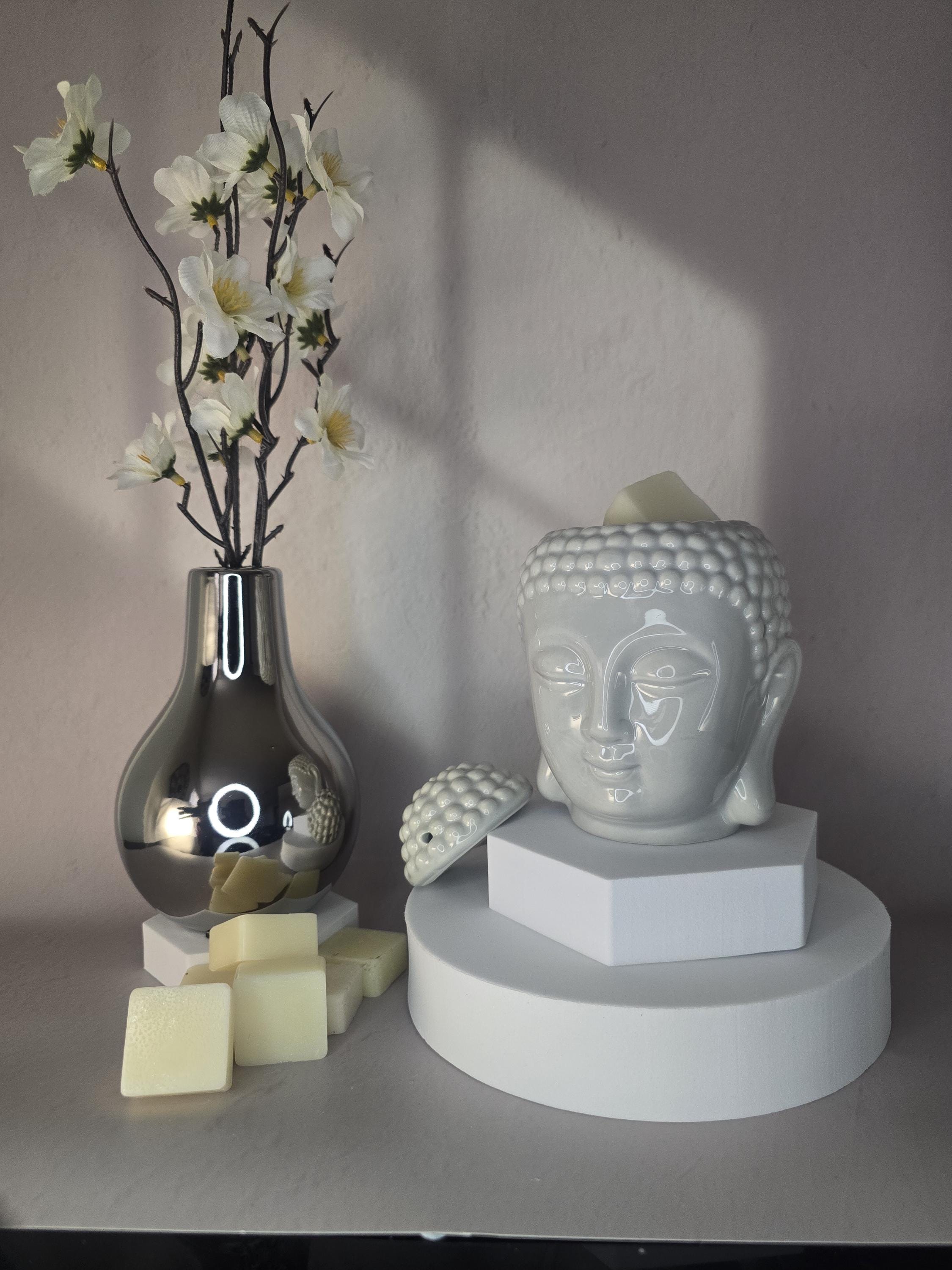 Decorative setup with a vase, flowers, and a Buddha head sculpture on a neutral background