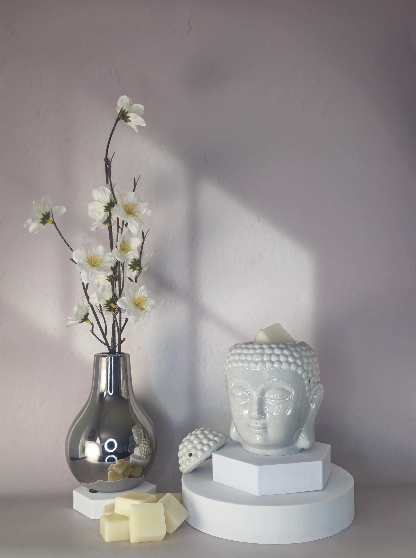 Decorative setup with a vase of flowers, a Buddha head sculpture, and candles on a neutral background